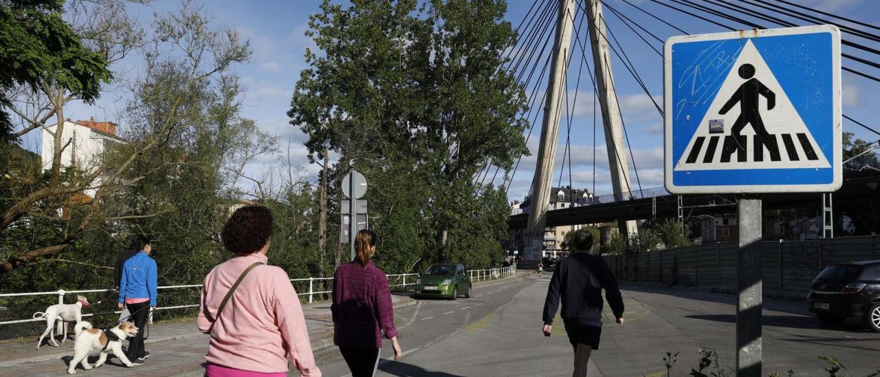 Vecinos caminan por el paseo de Los Llerones de Sama, con el puente atirantado al fondo. | Juan Plaza