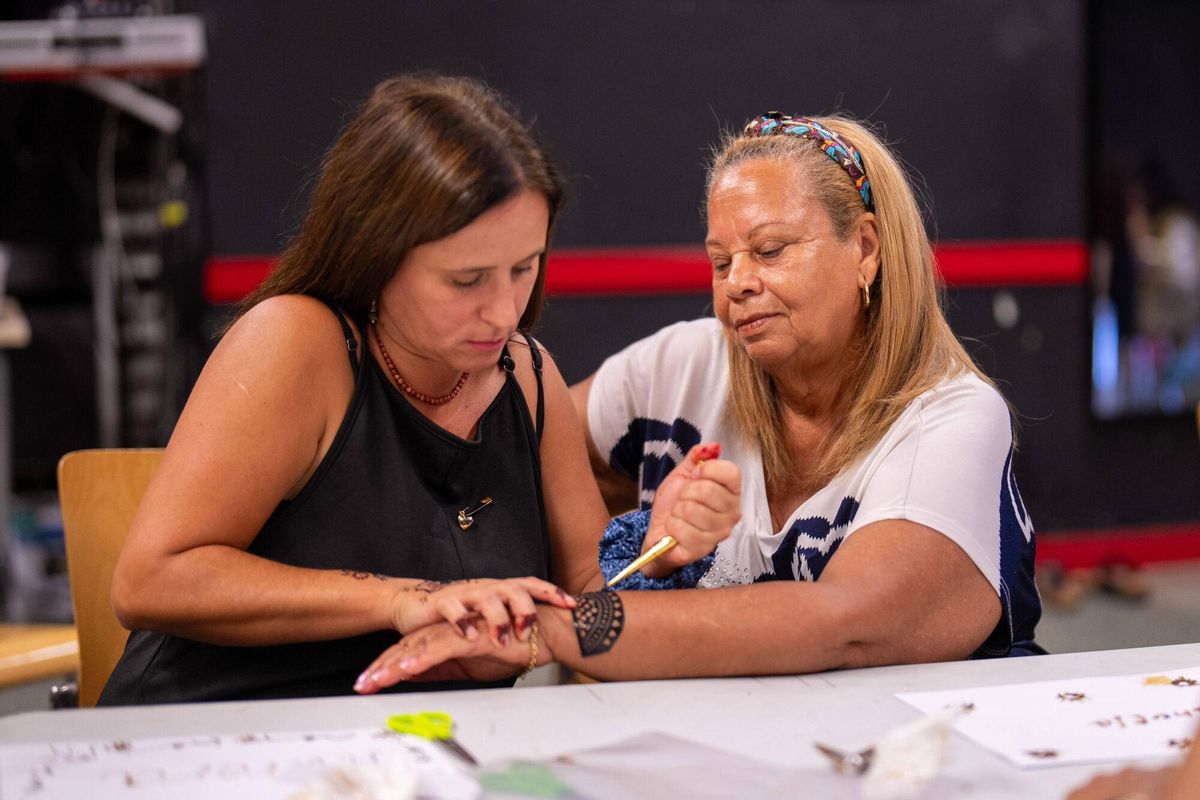 Un grupo de mujeres de entre 20 y 80 años, vecinas del barrio de la Trinitat Vella y usuarias del Centre de Vida Comunitària, participan en un taller de henna dentro de un casal de verano femenino.