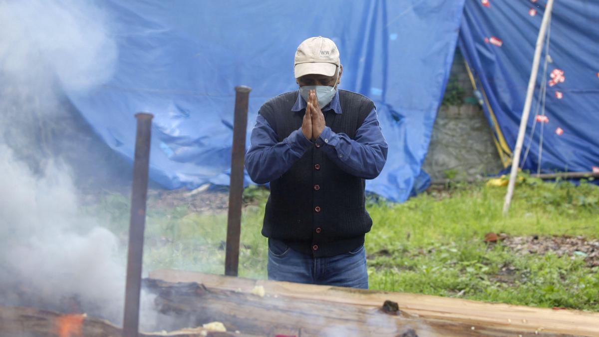 Un hombre reza junto al féretro de una persona muerta en la India por COVID.