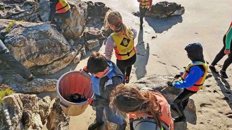 Alumnas de la escuela de vela muestran plásticos en la playa. // David Fontán