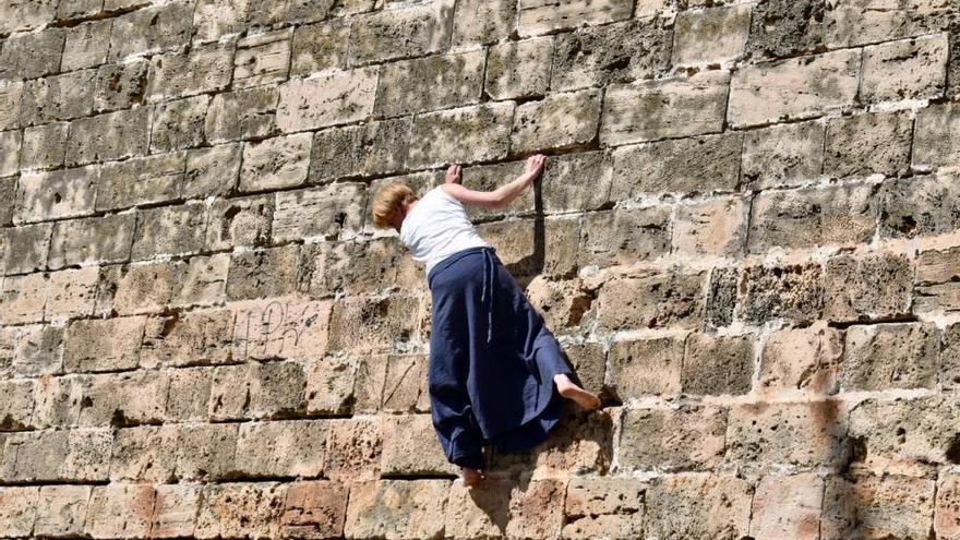 Una turista practica la escalada en las murallas de Palma descalza y con falda