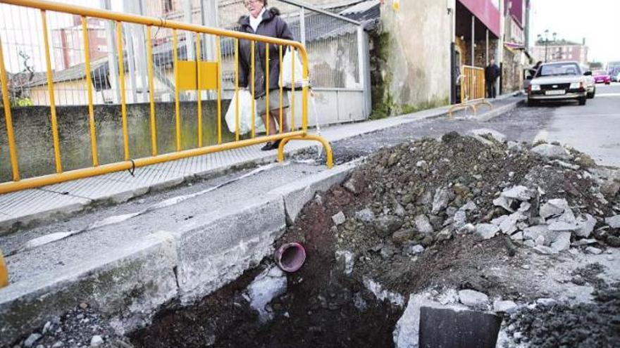 Una mujer sortea las obras, ahora paralizadas, e intenta pasar cargada con bolsas por las aceras estrechadas de La Corredoria.