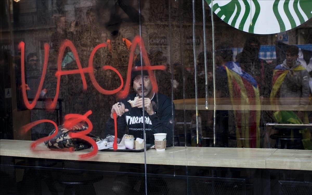 Un hombre come un bocadillo en una cafeteria de Barcelona mientras contempla en paso de la manifestación independentista.