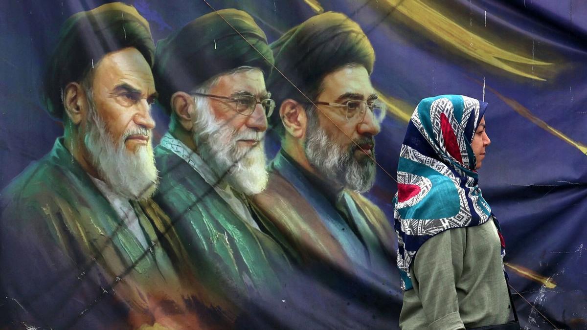 Una mujer pasa frente a un cartel con los rostros de los líderes supremos Ruhollah Jomeini, Alí Jameneí y Mojtaba Jameneí, este jueves en Teherán.