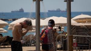 Varias personas se mojan en las duchas de la playa de la Barceloneta.