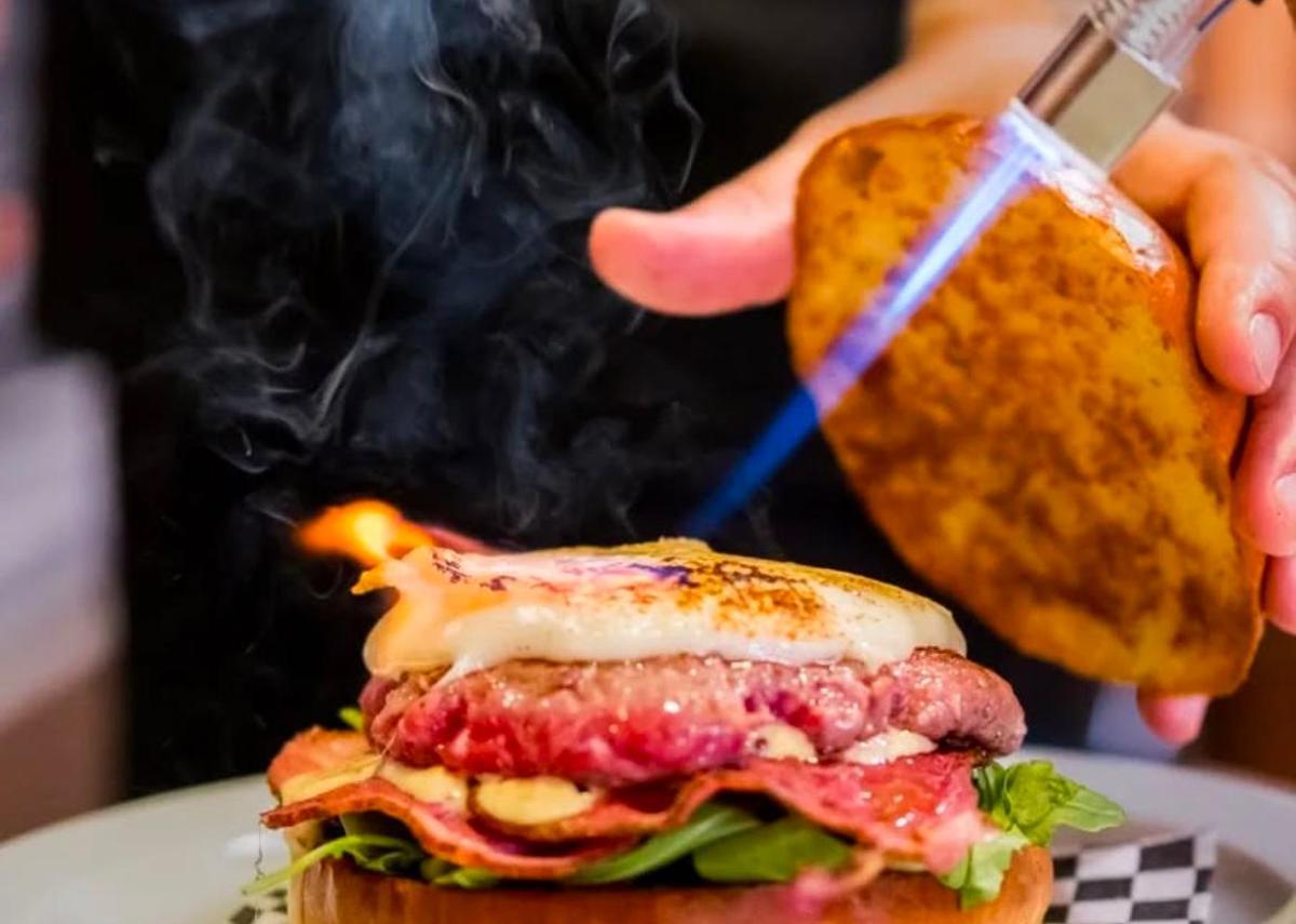 Una hamburguesa siendo flambeada por encima con un soplete especial de cocina