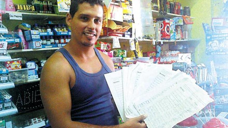 Remi, propietario de una pequeña tienda junto a la plaza de San Juan, mostrando las 280 firmas recogidas en su negocio.