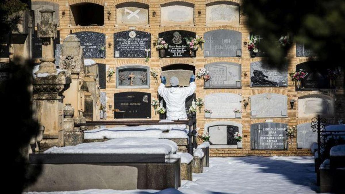 Un hombre coloca una lápida en el cementerio de Torrero de Zaragoza ataviado con un equipo de protección contra el covid-19.
