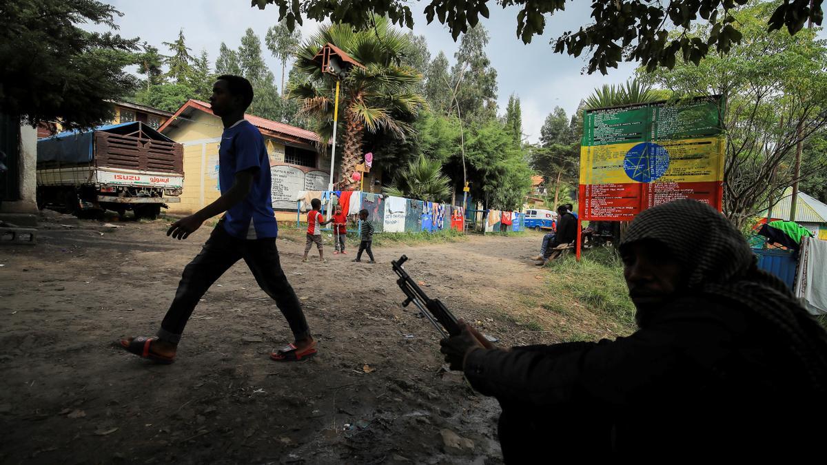 Un miembro de la seguridad privada se sienta con un arma mientras los niños juegan en un campamento para desplazados internos debido a los enfrentamientos entre la Fuerza Nacional de Defensa de Etiopía (ENDF) y las fuerzas del Frente Popular de Liberación de Tigray (TPLF) en la ciudad de Dessie, región de Amhara, Etiopía.