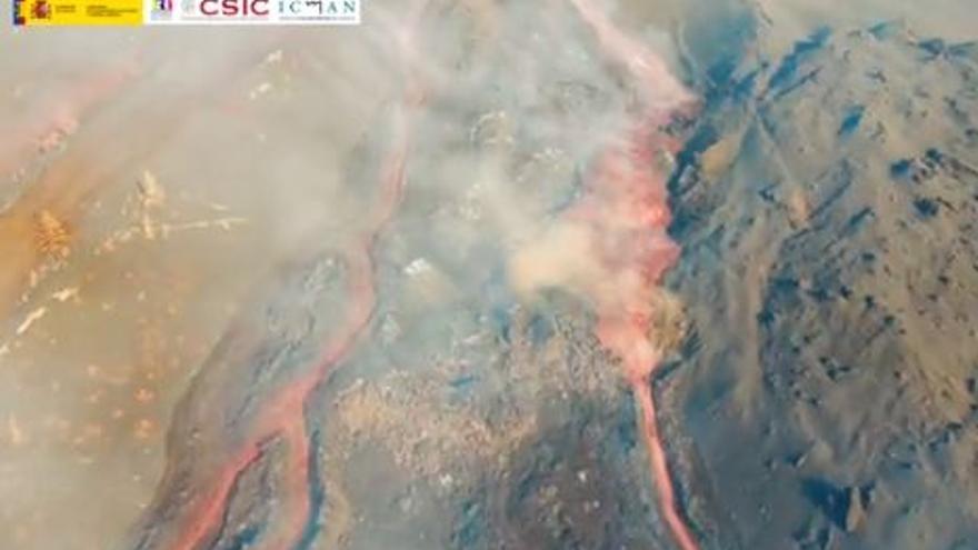 Vista de dron remontando la colada del volcán de La Palma, que fluye hacia el mar, y panorámica de la boca principal, en plena actividad efusiva y eruptiva.