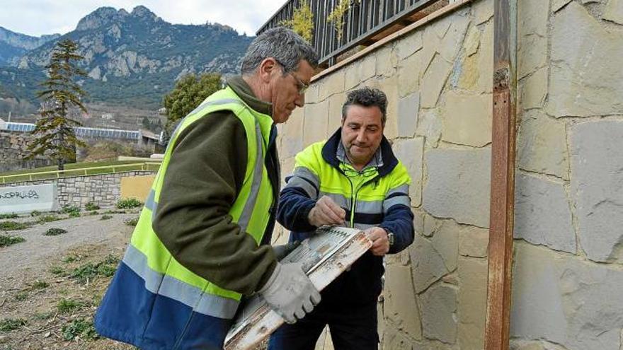 Dos operaris de les brigades municipals recol·locant la placa de la plaça de Mossèn Armengou, ahir