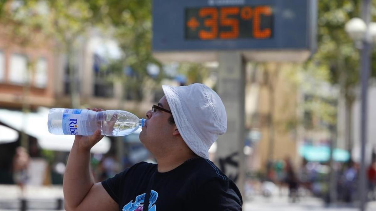 Un hombre se refresca ante un termómetro que marca 35 grados, en Barcelona.