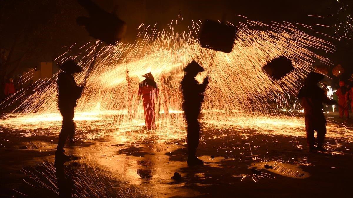 Artistas populares con linternas actúan bajo la lluvia de chispas de hierro fundido durante una celebración local antes del Festival de Linternas Chinas en la provincia de Luzhou Sichuan.