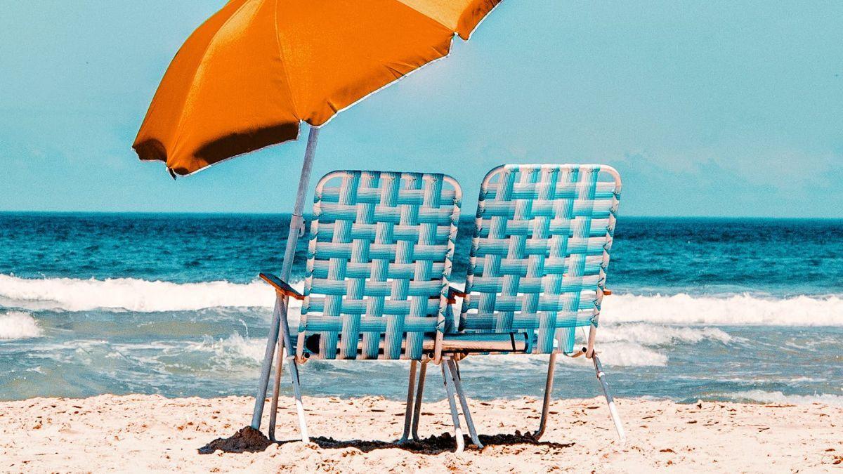 Una silla de playa con sombrilla y una silla de playa en la arena.