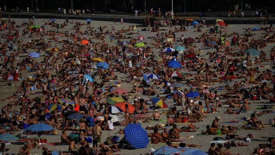 Decenas de personas toman el sol en un día de verano en la playa coruñesa de Riazor.