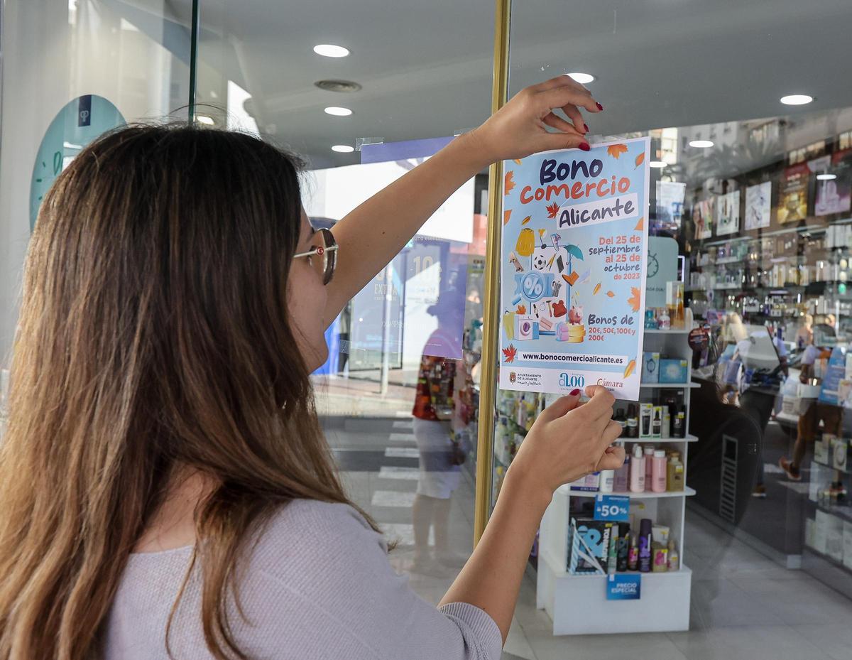 La trabajadora de una perfumería coloca el cartel del Bono Comercio en la puerta.