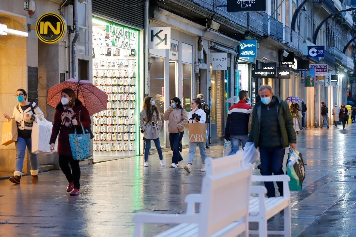 Varias personas pasean con mascarilla por una calle comercial.