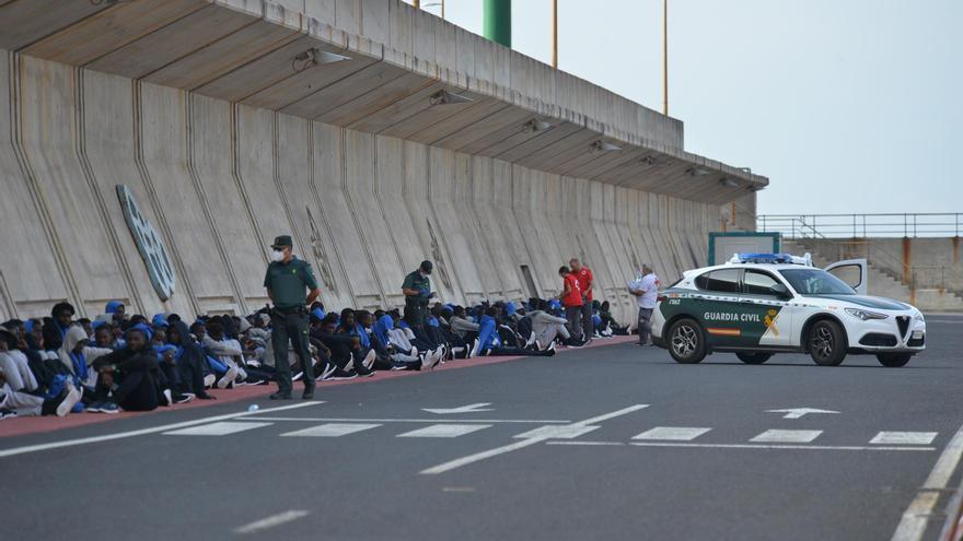 Un vehículo y agentes de la Guardia Civil al lado de los migrantes que esperan a ser trasladados, en el muelle de la Restinga, a 11 de septiembre de 2023, en El Hierro, Canarias (España). En la mañana de hoy se ha procedido al traslado de más de 400 inmig