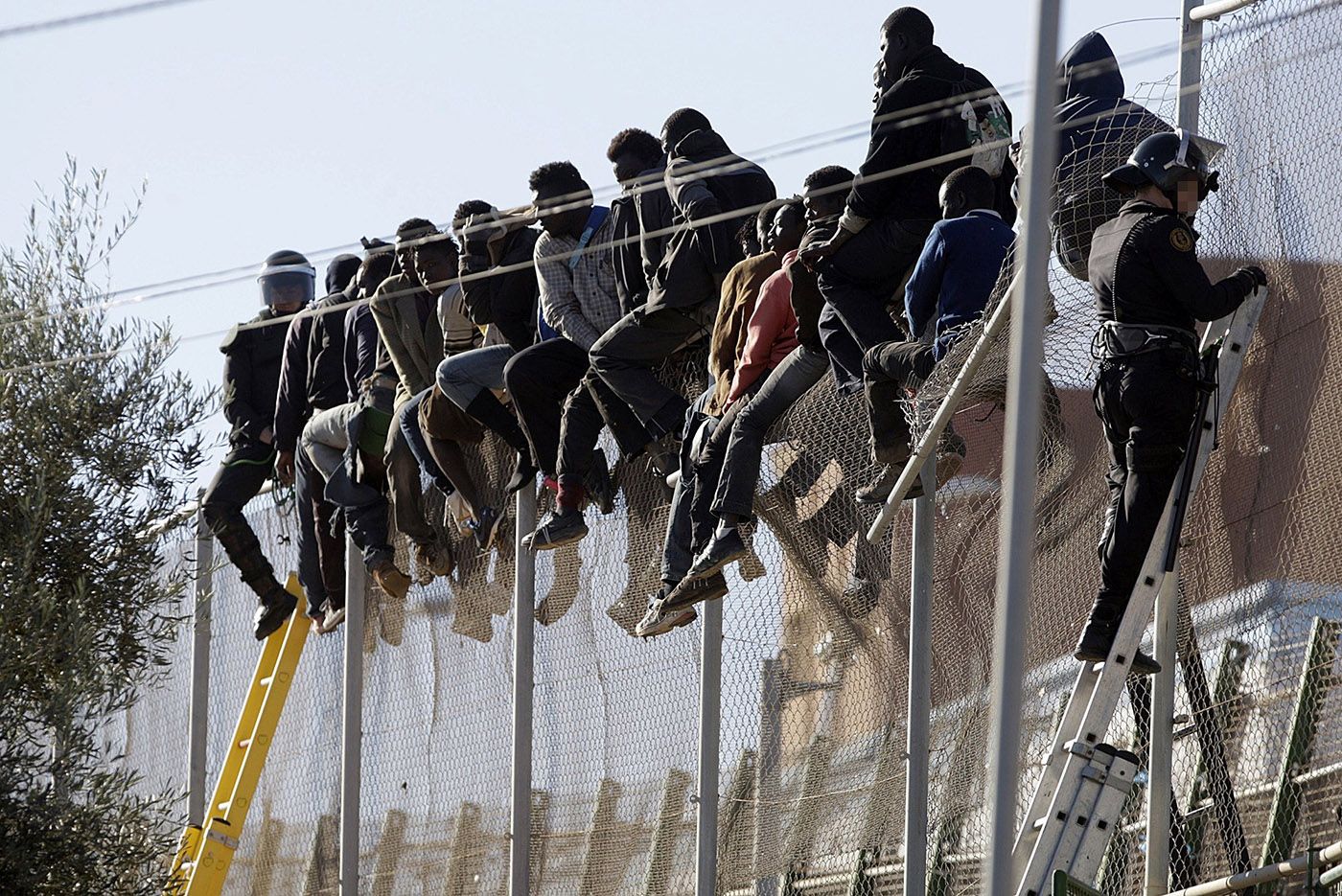 Personas migrantes sobre la valla de Melilla intentando cruzar la frontera