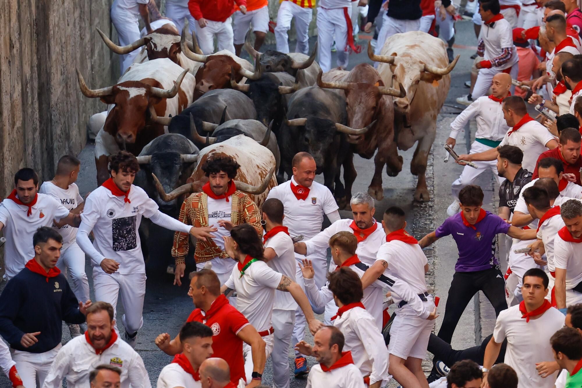 PAMPLONA, 12/07/2025.- Mozos perseguidos por los toros de la ganadería de José Escolar en el sexto encierro de los Sanfermines, este sábado en Pamplona. EFE/Jesús Diges