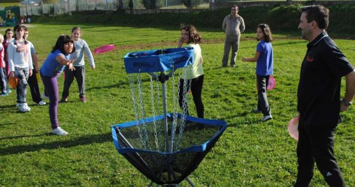 Alumnos de sexto de Primaria juegan al "disc golf" bajo la supervisión de Carlos Río, a la derecha.