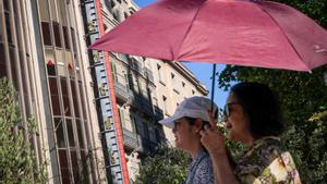 Unas mujeres se refugian del sol bajo un paraguas durante un viernes de altas temperaturas en Barcelona.