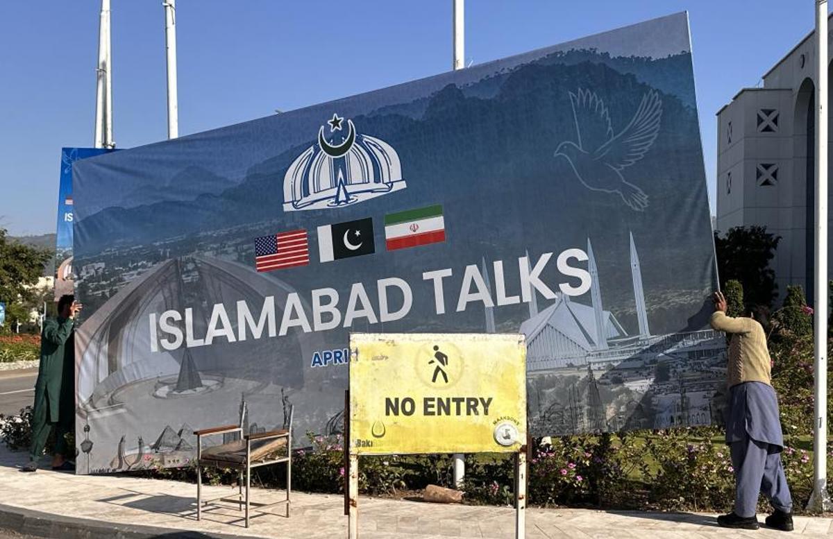 Un operario retira un cartel sobre las conversaciones de paz entre EEUU e Irán en Islamabad.
