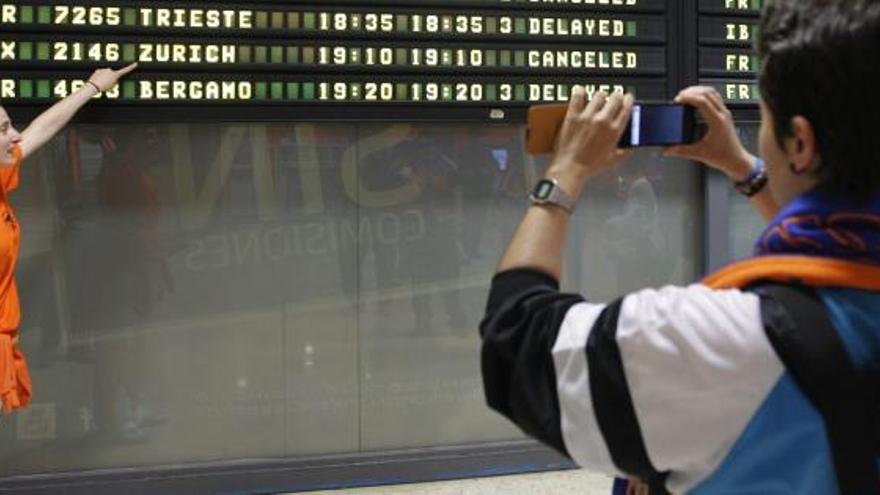 Aficionadas del Ros Casares, que el domingo ganó Euroliga de baloncesto femenina, se fotografían junto a un panel del aeropuerto de Manises mientras señalan la cancelación del vuelo que iba a traer de regreso a Valencia a las jugadoras del club