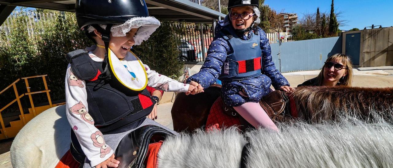 Dos alumnas del colegio de Educación Especial Tomàs Llàcer se dan la mano en una sesión de equinoterapia