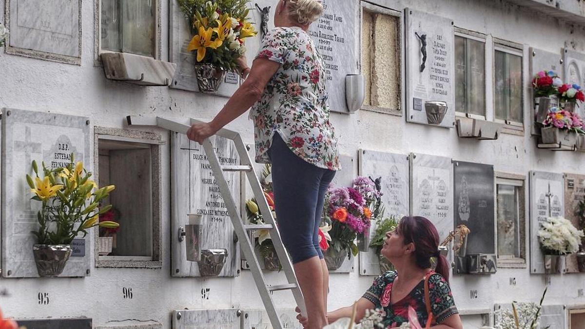 Dos mujeres ponen flores en un nicho del cementerio de Santa Lastenia.