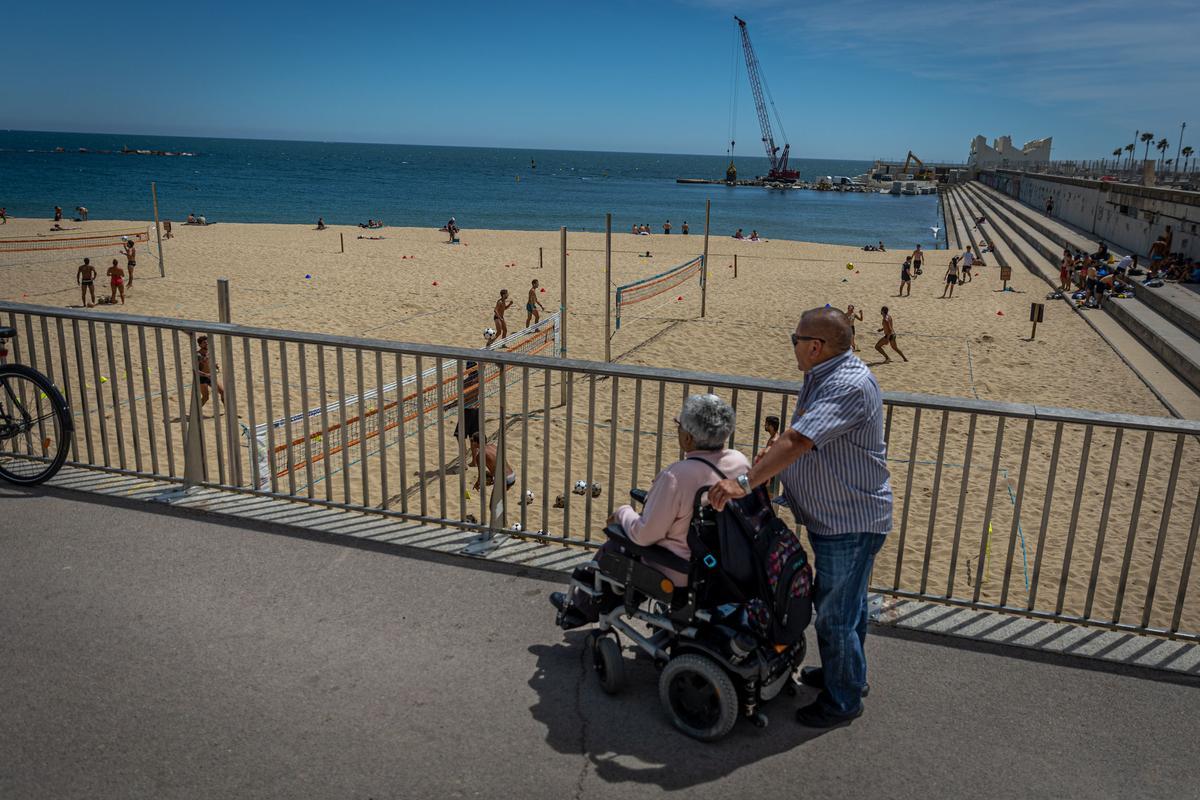 Basi Torre, en silla de ruedas, y Custo Rosales, en el paseo junto a la playa de Nova Icària, en Barcelona.