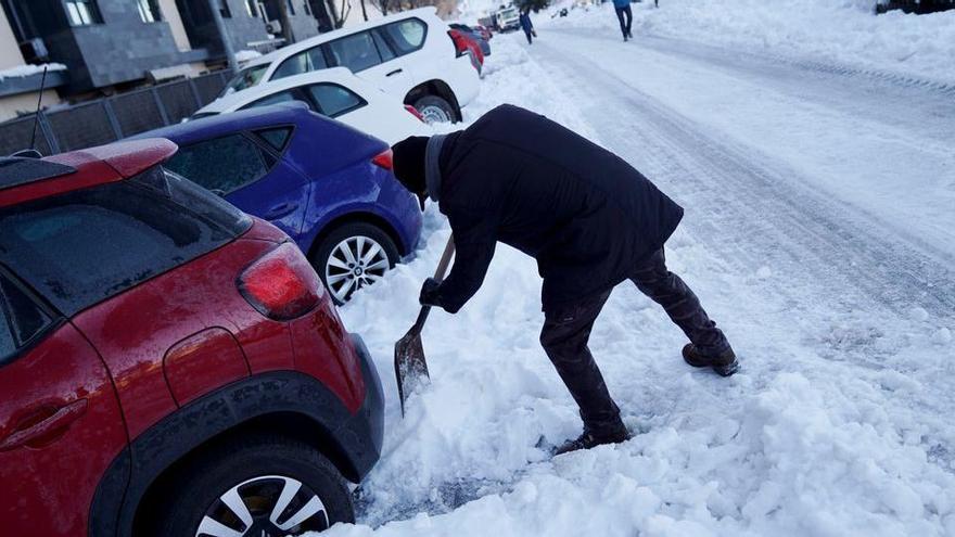 Una persona quita nieve para poder sacar el coche e ir a trabajar.