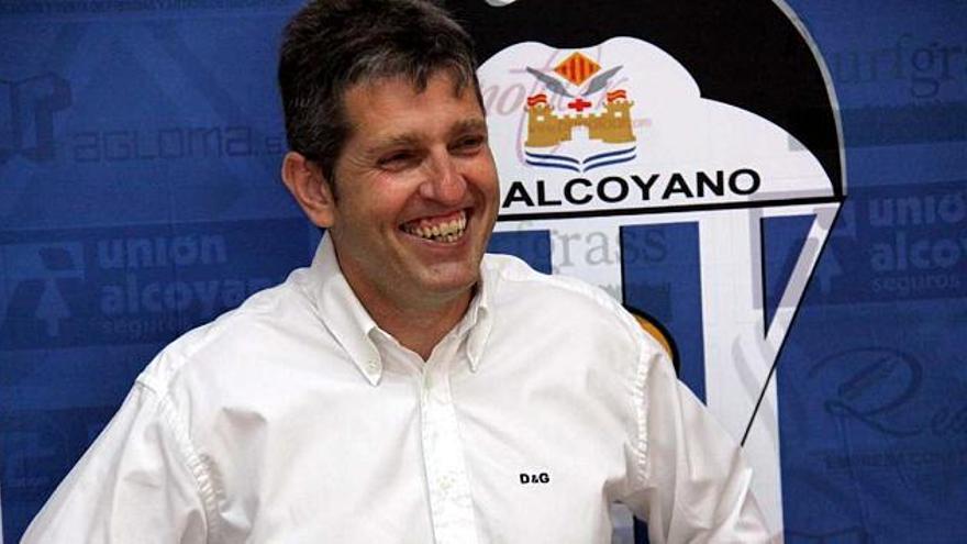 El presidente del Alcoyano, Juan Serrano, sonríe delante del escudo del club.