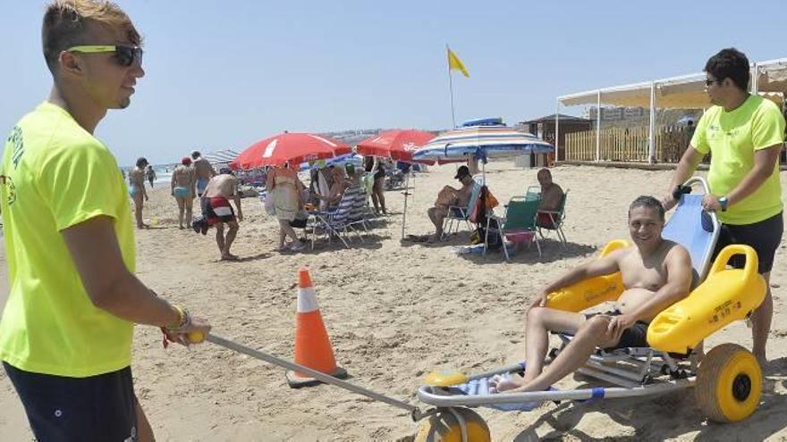 Dos socorristas con un usuario del servicio de baño accesible en la playa de Arenales.