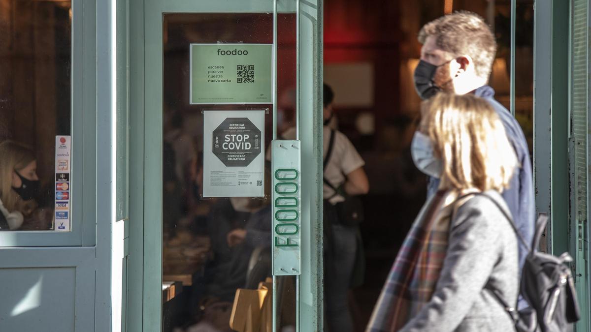 Dos persona con mascarilla pasan por delante de un restaurante que exige el pasaporte Covid.