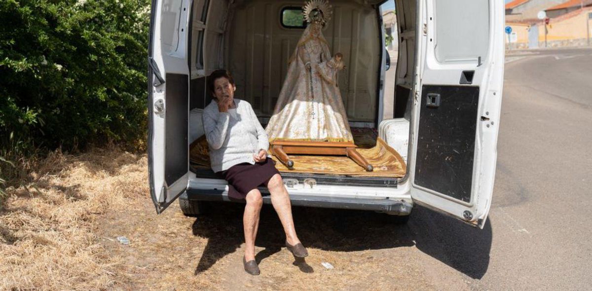 Una mujer come una pasta a la sombra de la furgoneta de la Virgen del Rosario de Villarrín, antes de comenzar la procesión. | Emilio Fraile