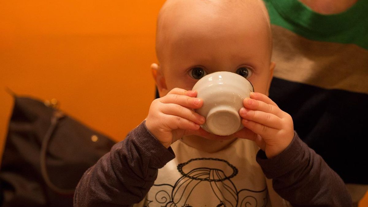 Un bebé bebe de una taza