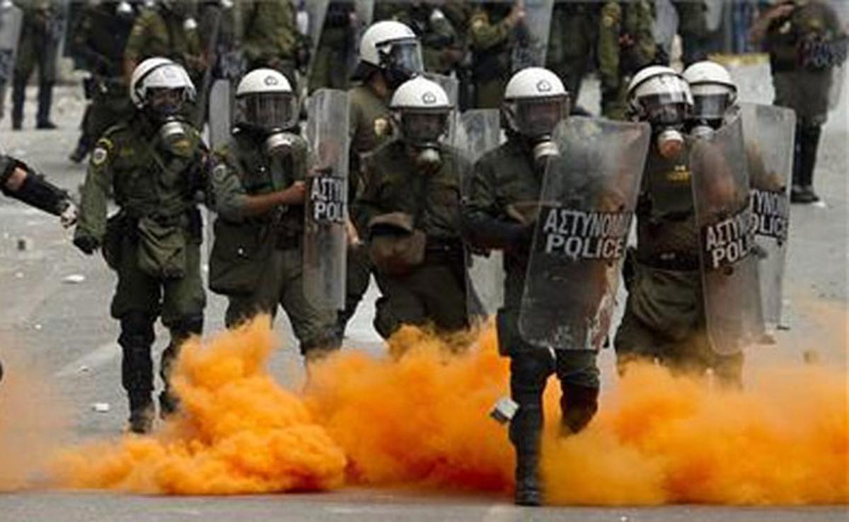 Agents antiavalots s’estan enmig d’un núvol taronja de gas lacrimogen durant els enfrontaments entre protestants i policia.