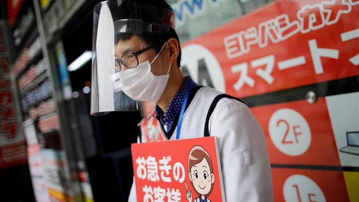 Un empleado de una tienda de electrónica usa mascarilla protectora en una calle de Tokio.