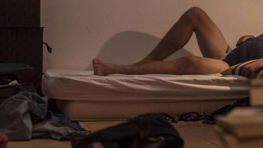 Las piernas de un hombre sobresalen de un colchón en un piso, en una foto de archivo.