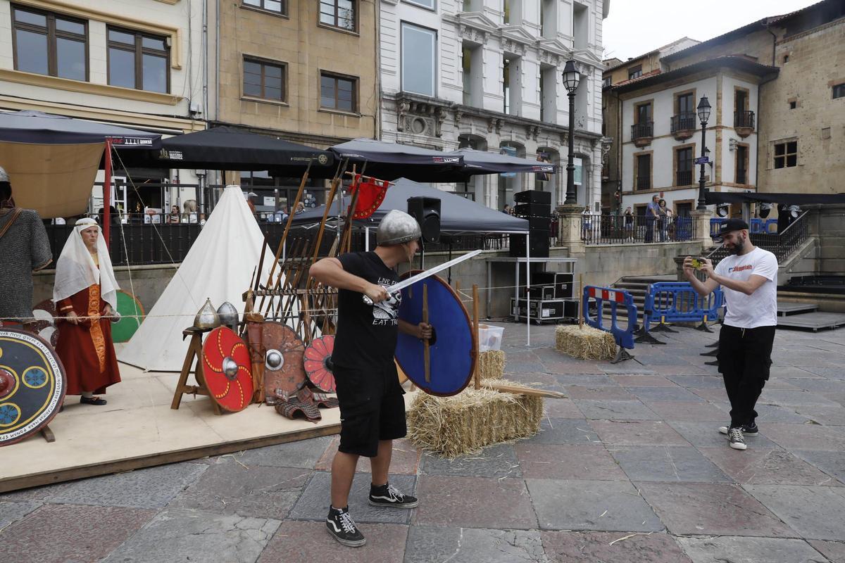 Un visitante toma una fotografía a otro que porta escudo, casco y espada.