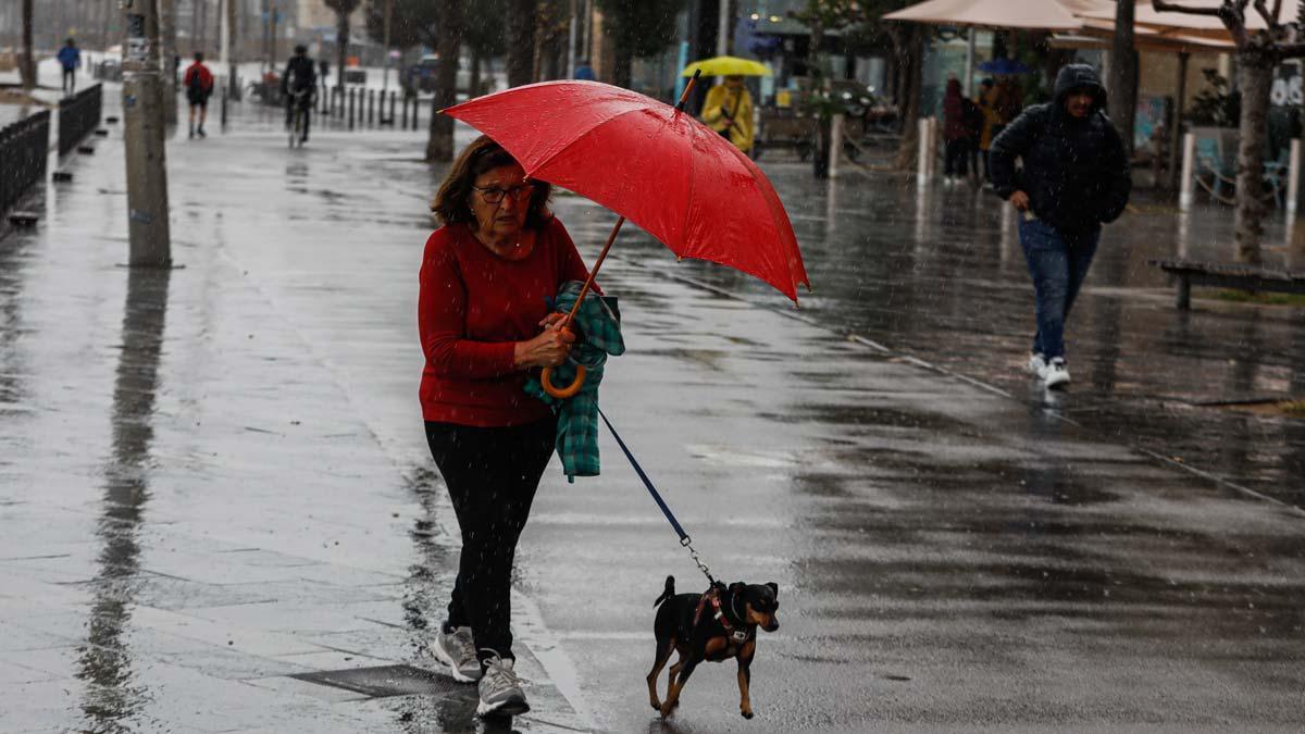 Una mujer se resguarda de la lluvia en la Barceloneta, tras la llegada de la borrasca Blas
