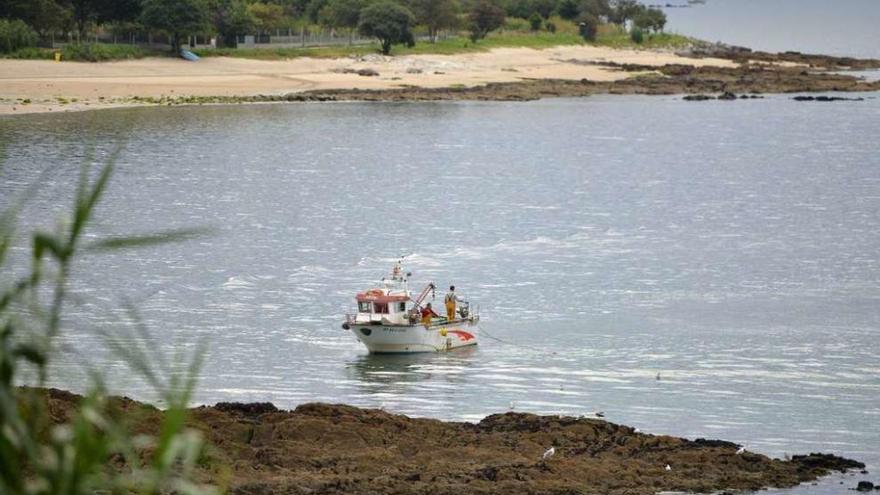 Una embarcación marisquea a flote en playa de O Laño, en Samieira. // Gustavo Santos