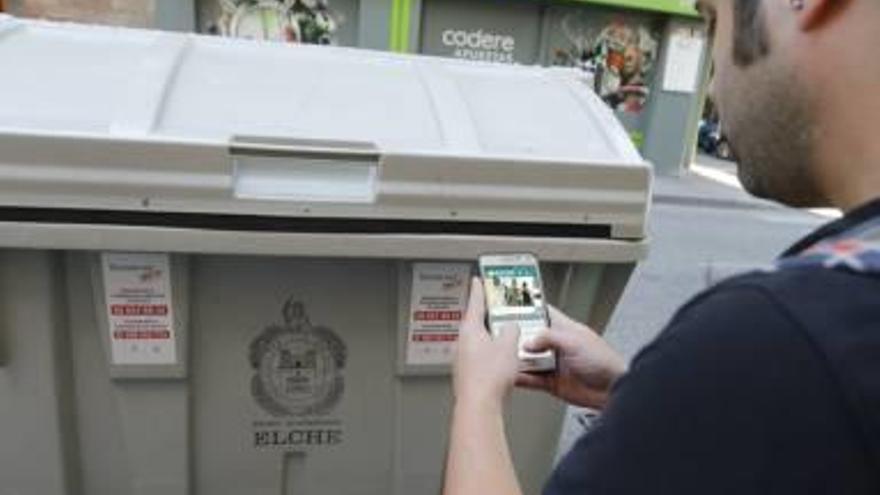 Un joven con su teléfono móvil frente a un contenedor de basura en Elche.