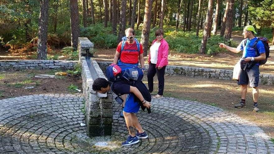 Unos peregrinos se refrescan en el lavadero de pies rehabilitado en la parroquia de Saxamonde. // FdV