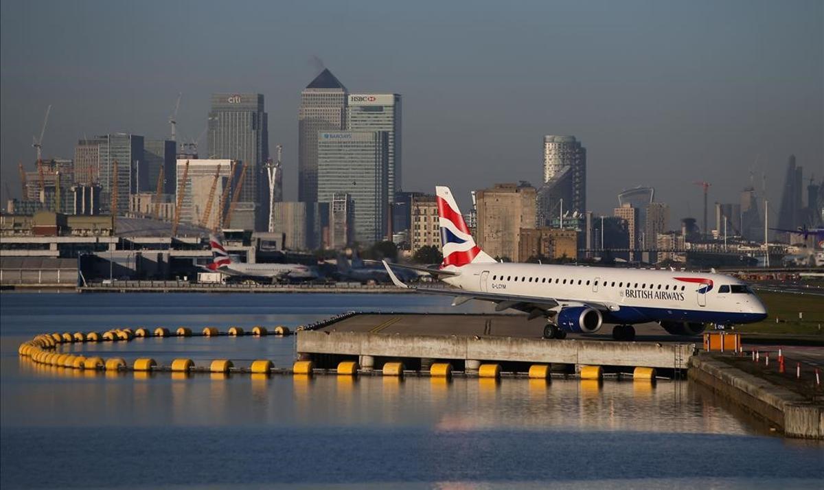 (FILES) This file photo taken on October 27  2017 shows a British Airways airplane waiting on the runway with the towers and buildings of London s Canary Wharf financial district in background before taking off at London City Airport in London  - Germany is considering banning flights from Britain and South Africa to prevent the spread of new  more infectious coronavirus strain circulating in the two countries  a source close to the German health ministry told AFP on Sunday  December 20  2020  (Photo by Daniel LEAL-OLIVAS   AFP)