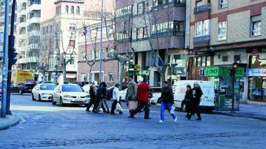 Viandantes cruzan una calle de la avenida Tres Cruces con sus compras.