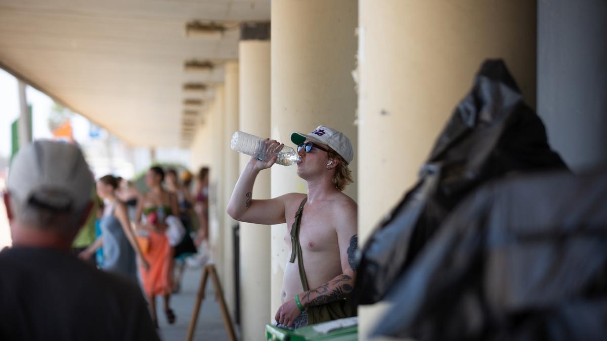 Un chico sin camiseta bebe agua en el parque de la Barceloneta en julio.