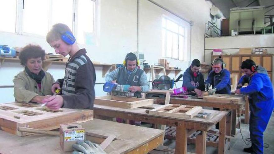 aprendices de carpinteros en el taller. En primer término, Diego Feito recibe las instrucciones de la profesora Margarita Llorente durante la fabricación de una ventana para las casas de madera que preparan para los colegios de Cornellana y La Espina.
