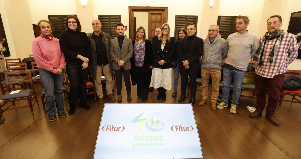 En el centro, Gimena Llamedo y Lara Rodríguez, viceconsejera de Turismo, junto a los empresarios, dirigentes y técnicos que participan en el programa en Fitur, posando en Gijón ante el logo del Paraíso Natural retocado por su autor con motivo del 40.º aniversario. | LUISMA MURIAS